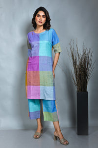 A person wearing a purple-blue checkered handwoven tunic with kantha detailing paired with matching wide-leg pants.