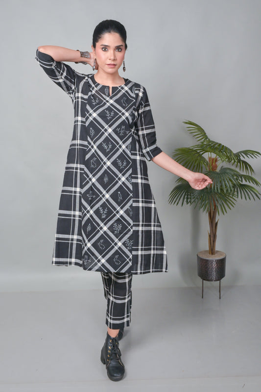 Woman wearing a black and white checkered dress standing next to a potted plant on a gray background