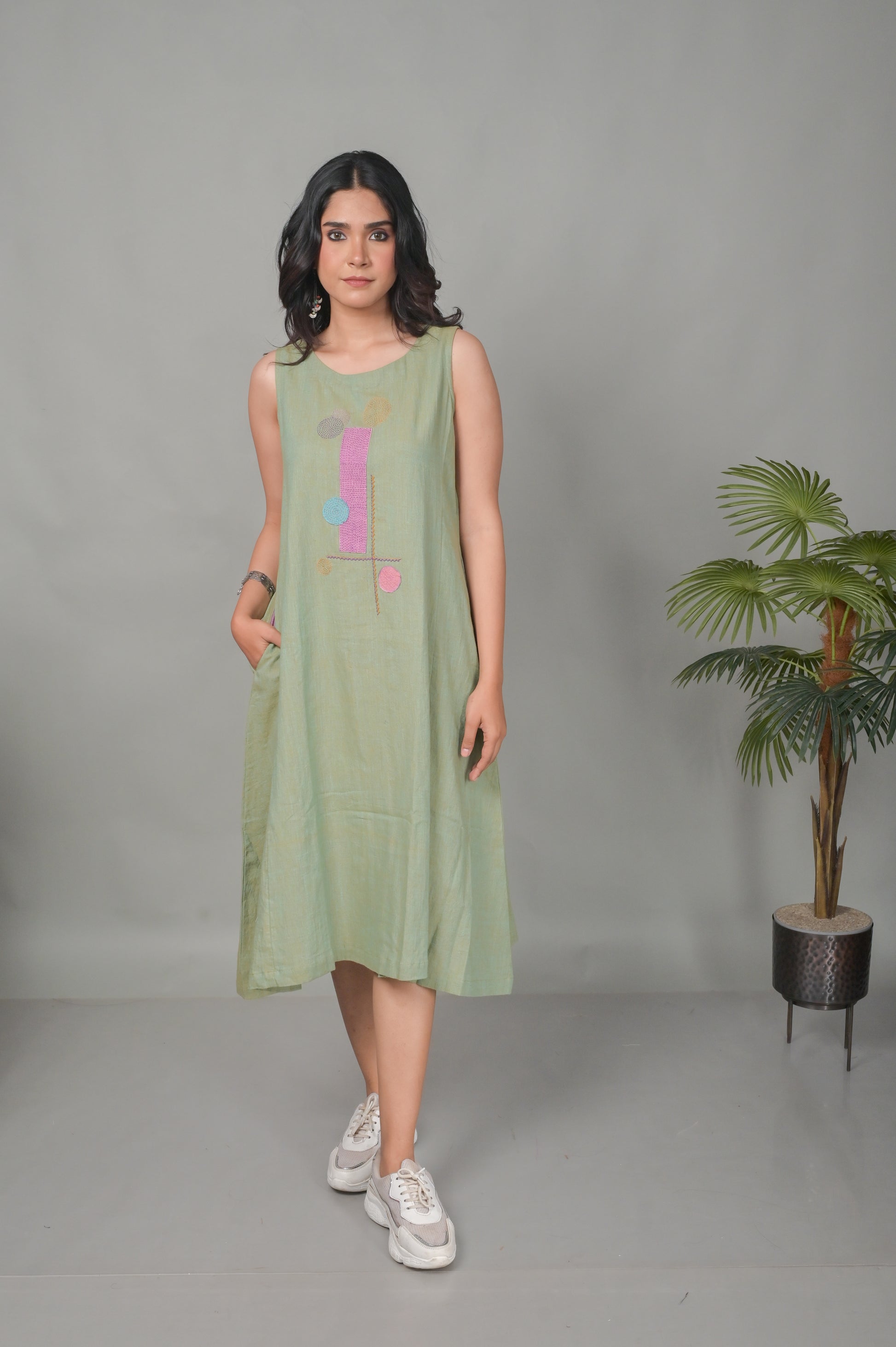 Woman wearing a light green sleeveless dress with colorful patterns, standing against a plain background.
