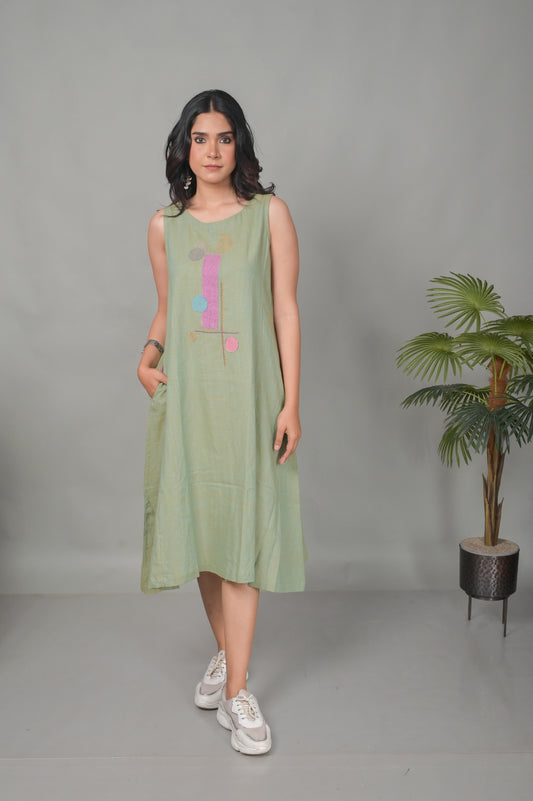 Woman wearing a light green sleeveless dress with colorful patterns, standing against a plain background.