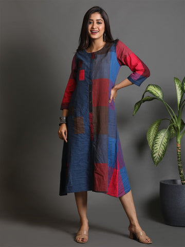 Woman wearing a colorful dress standing next to a plant against a gray background