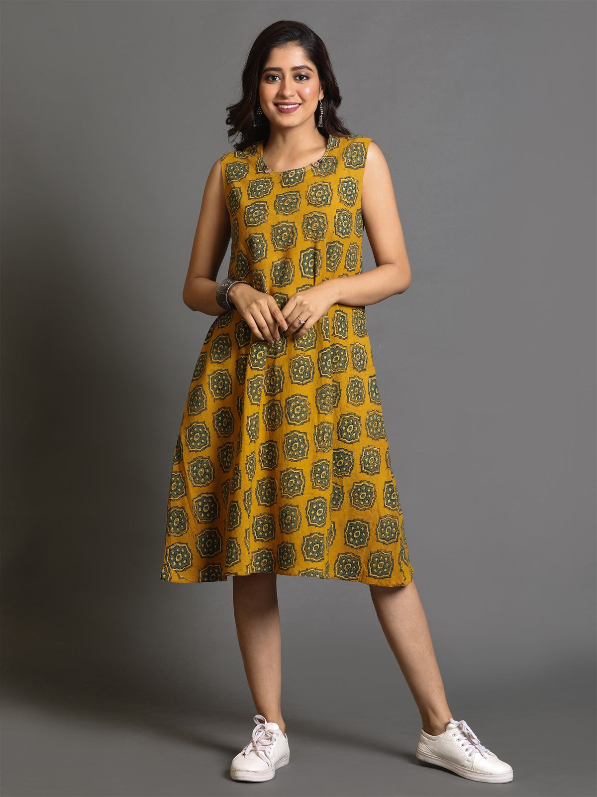 A woman posing in a mustard yellow Ajrakh block-printed dress with Kantha hand embroidery detailing, featuring a flared hem and three-quarter sleeves.