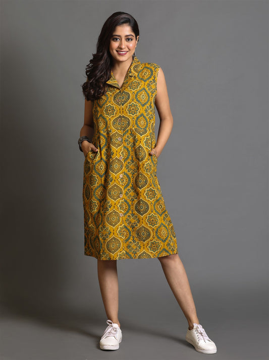 A woman posing in a mustard yellow Ajrakh block-printed dress with a double collar, showcasing the dress's pattern and fit.