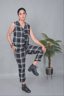 Woman wearing a black and white checkered outfit with boots, standing against a gray background with a plant.
