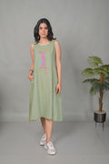 Woman wearing a light green sleeveless dress with colorful patterns, standing against a plain background.