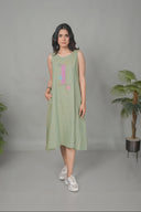 Woman wearing a light green sleeveless dress with colorful patterns, standing against a plain background.