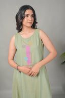 Woman wearing a light green sleeveless dress with colorful patterns on a gray background