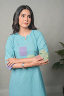 Woman wearing a light blue dress with colorful hand embroidery against a gray background