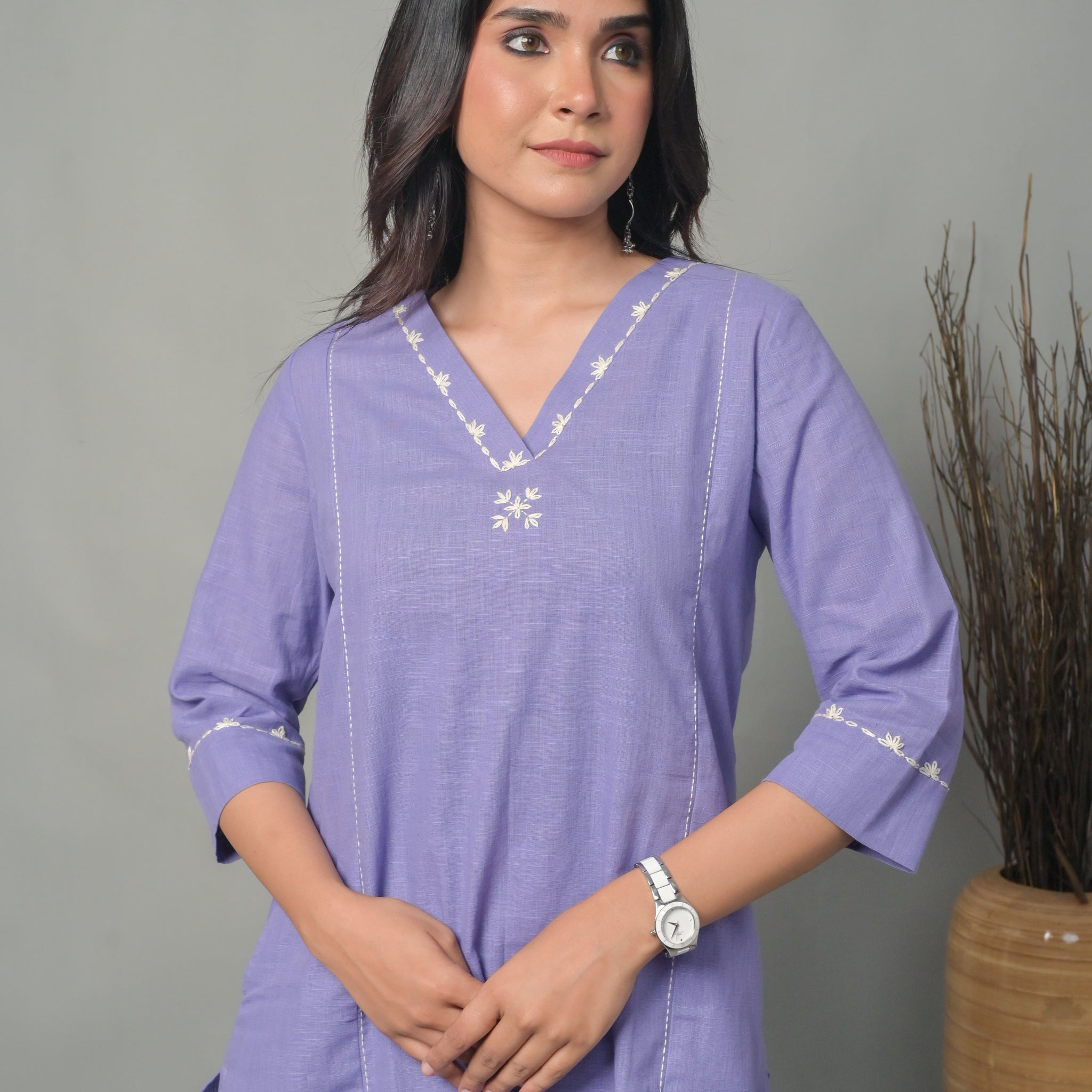 Woman wearing a purple dress with white embroidery against a gray background