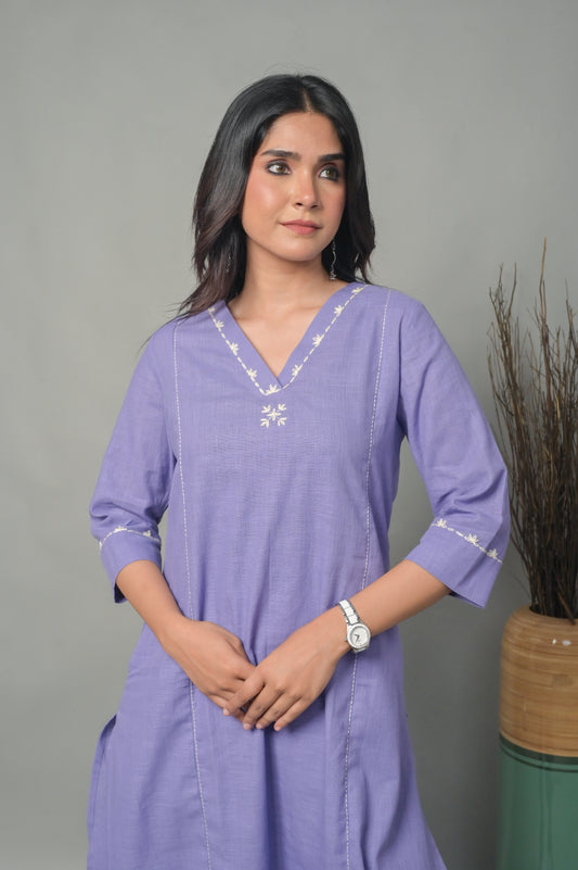 Woman wearing a purple dress with white embroidery against a gray background