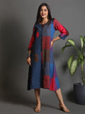 Woman wearing a colorful dress standing next to a plant against a gray background