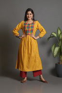 A woman posing in a yellow handwoven pleated kurta with multi-color checks on the yoke and mirror work on the chest.
